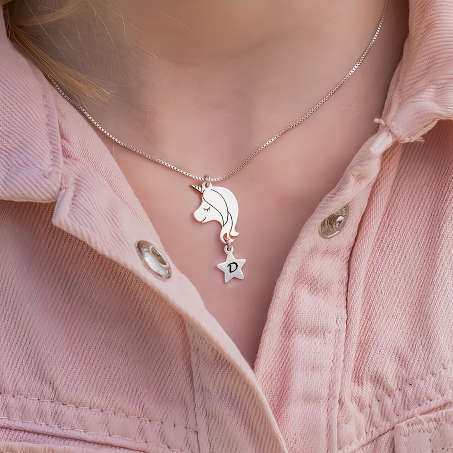 Close-up of a young girl wearing the silver personalized unicorn initial necklace on a pink jacket, showing the perfect size.