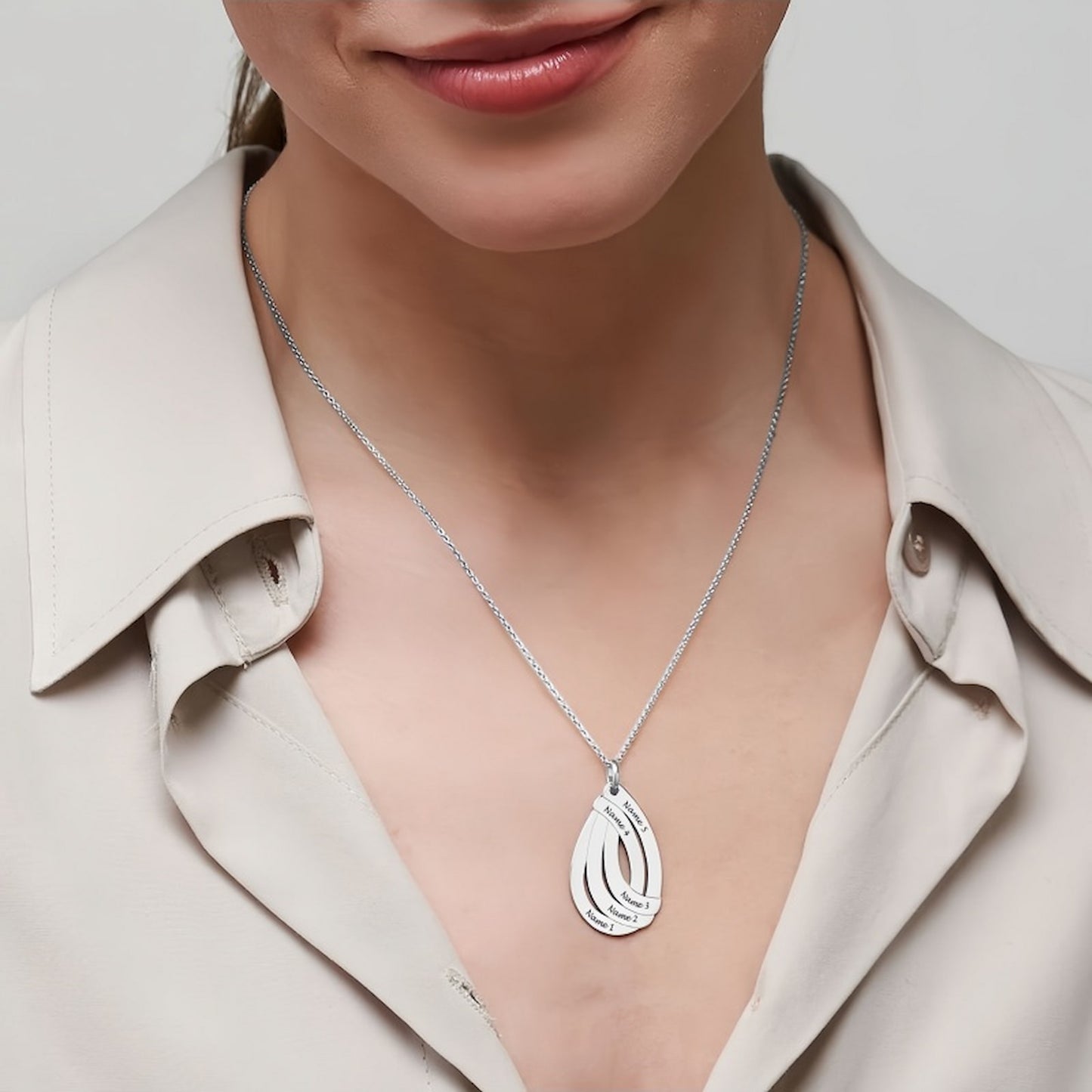Woman wearing silver personalized teardrop name necklace with multiple engraved names.