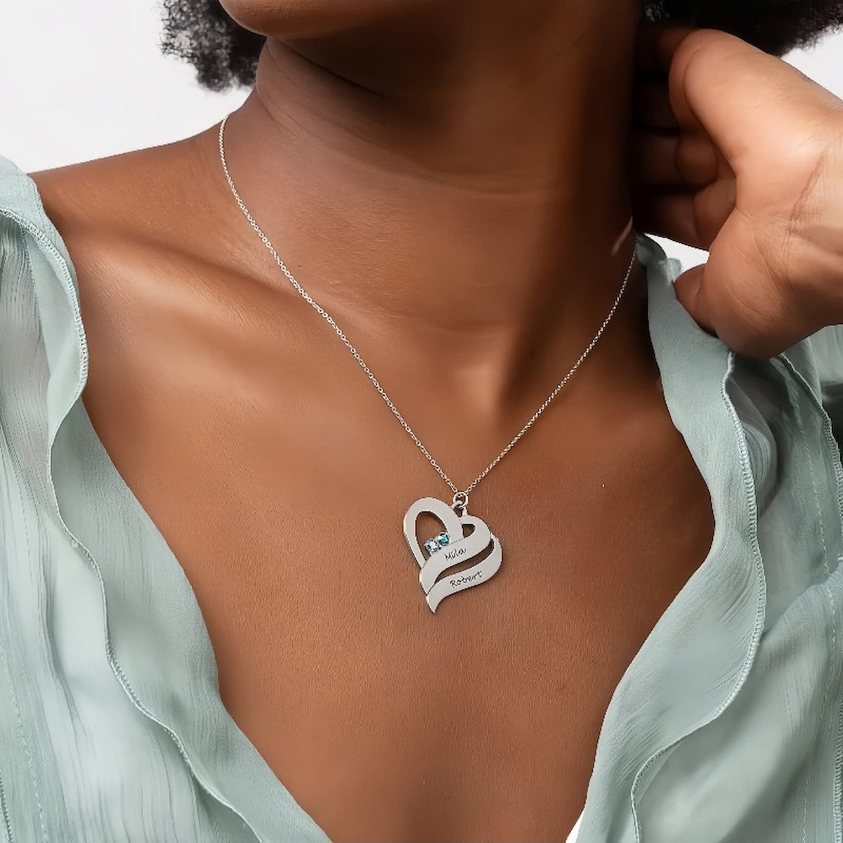 Model wearing the sterling silver two hearts necklace with custom names and birthstones over a light green blouse.
