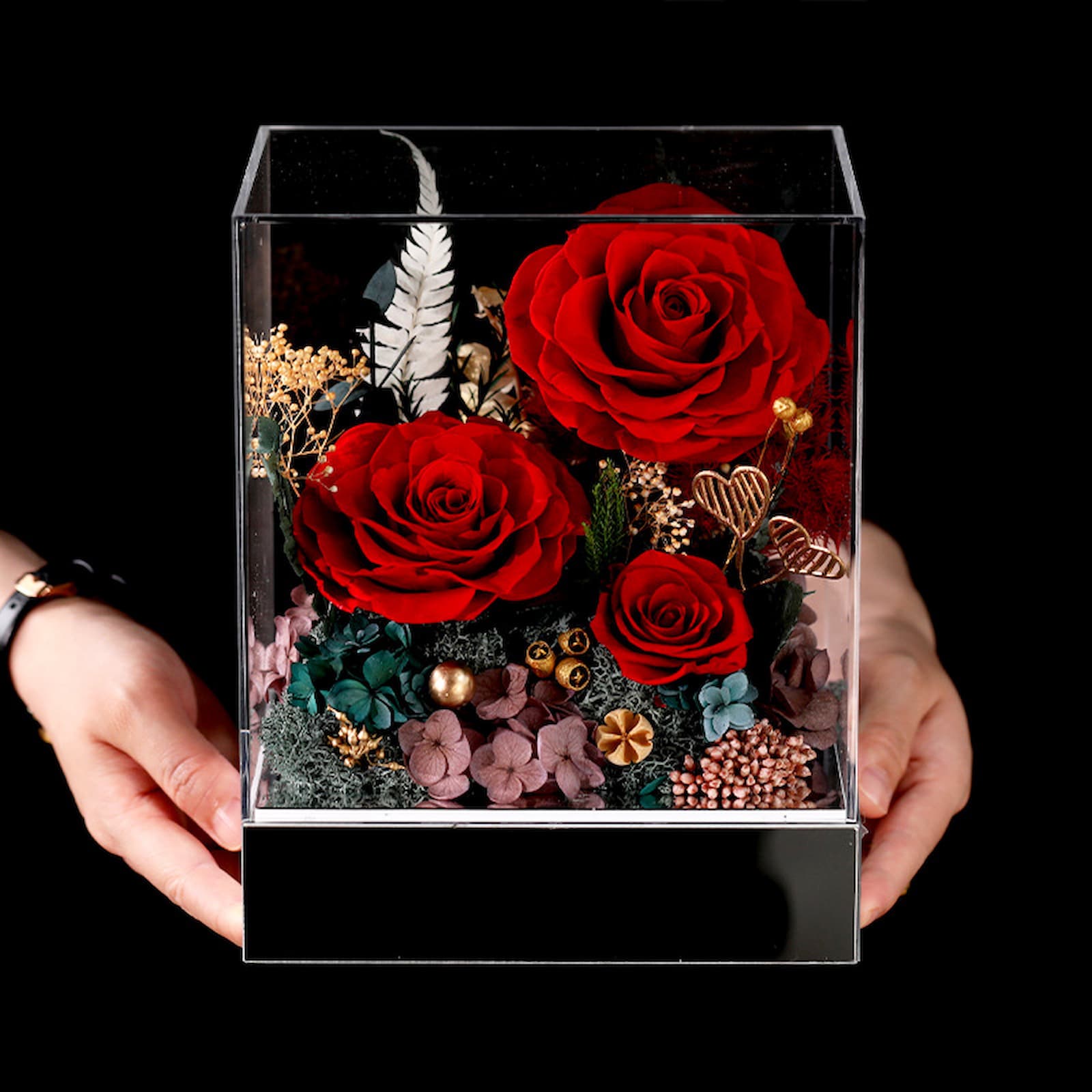 Close-up of an eternal flower arrangement featuring three vibrant red roses and surrounding pink and green filler flowers.