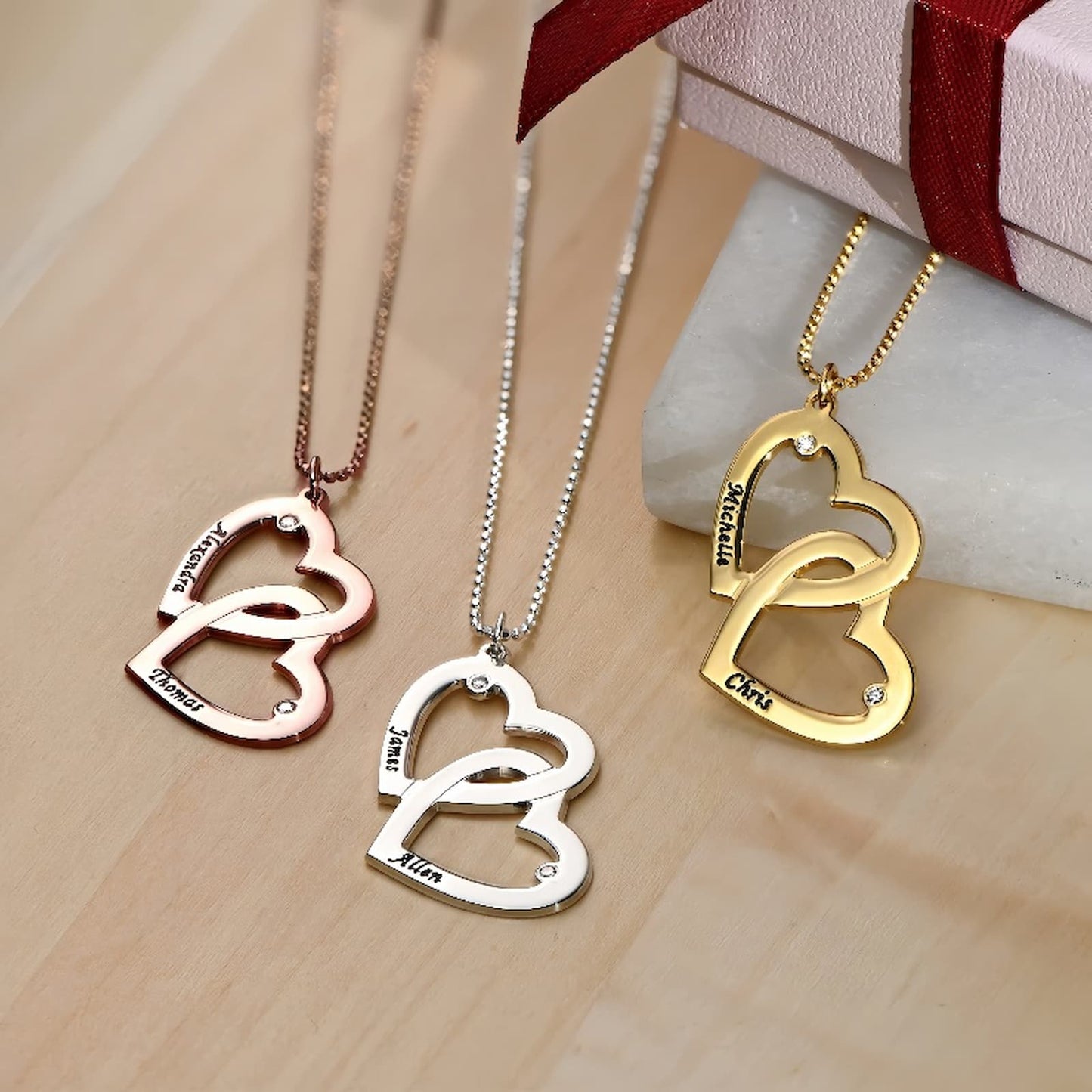 Custom heart-in-heart necklace featuring two cut-out names and simulated birthstones, available in silver, gold, and rose gold.