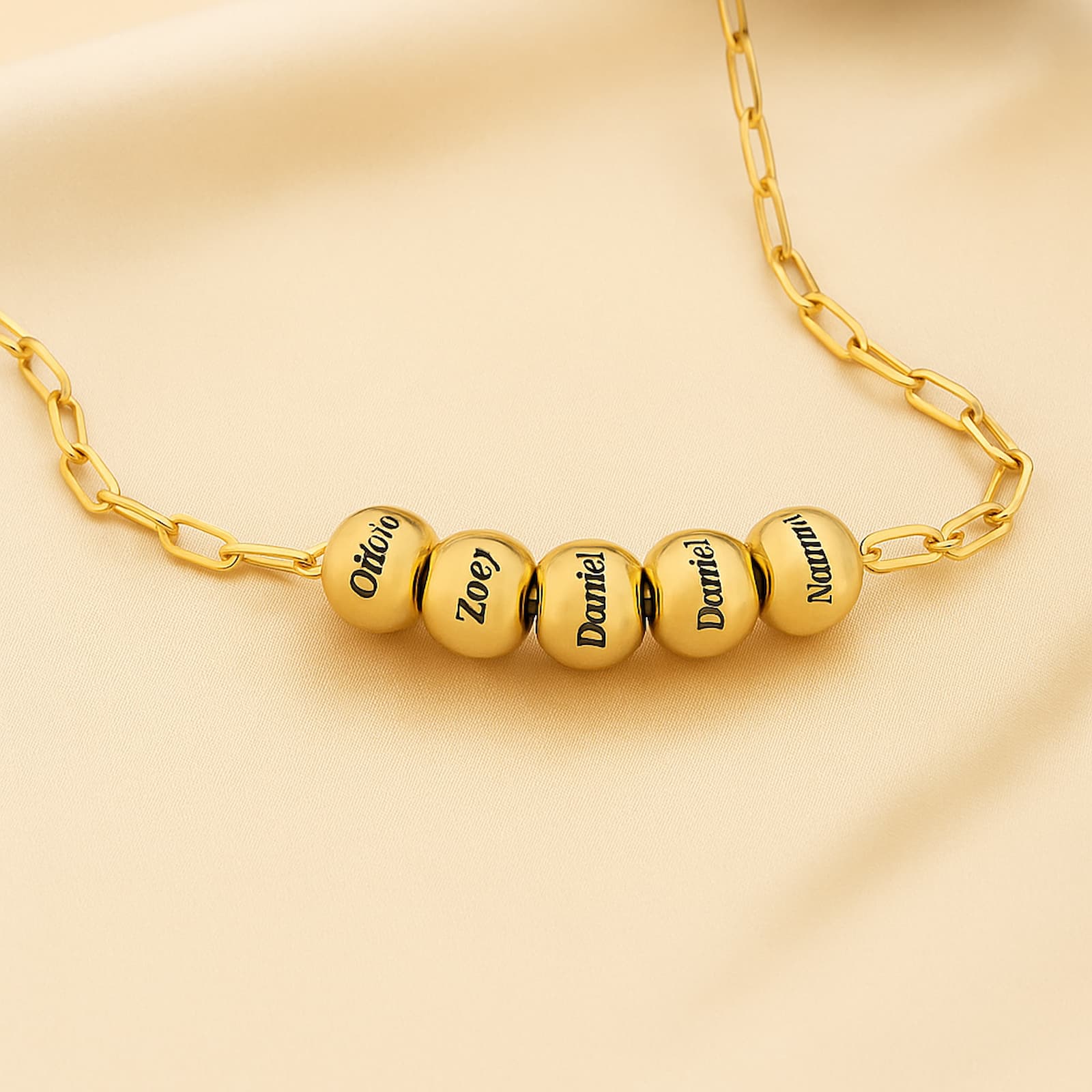 Close-up gold personalized name bead paperclip necklace. Engraved names on each bead.