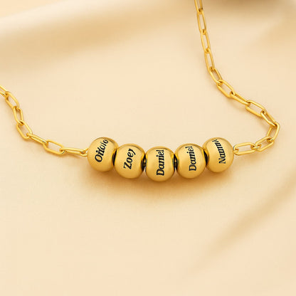 Close-up gold personalized name bead paperclip necklace. Engraved names on each bead.