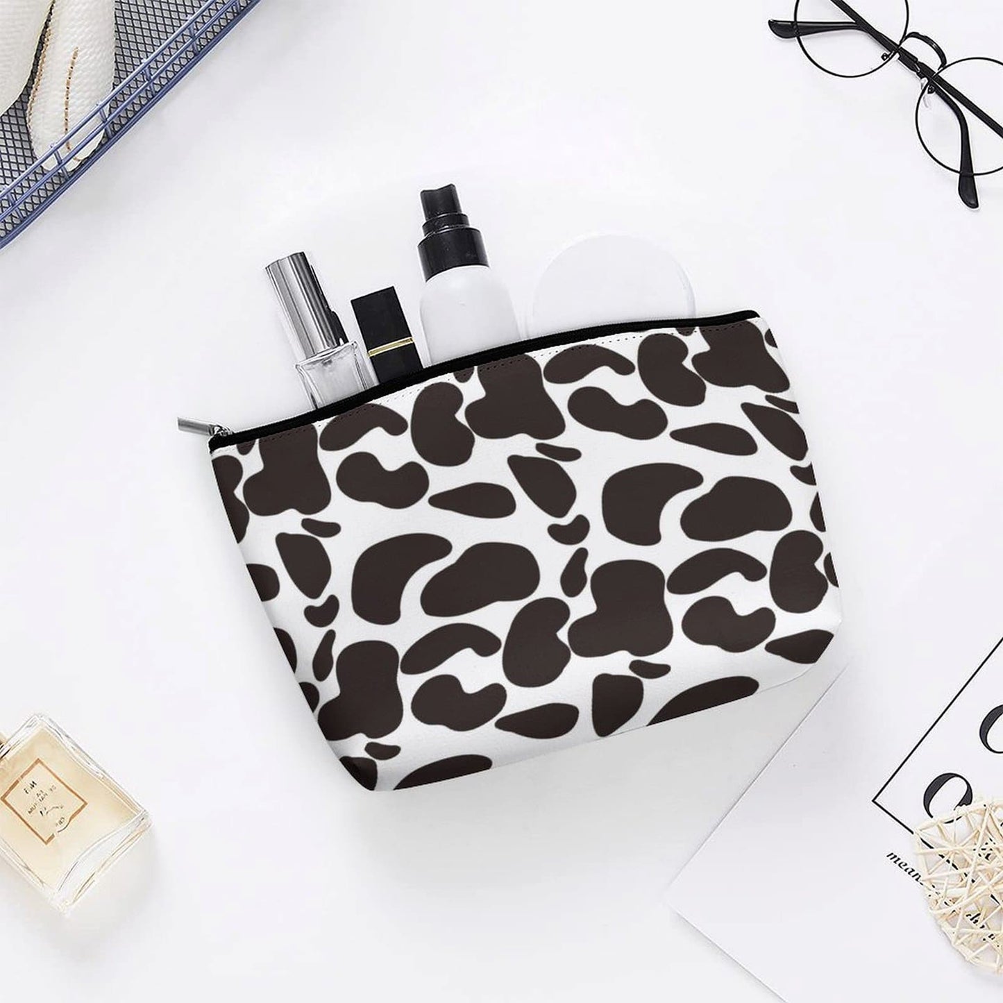 Cow Print Toiletry Bag on a white vanity, used for organizing small cosmetics, perfume, and glasses.