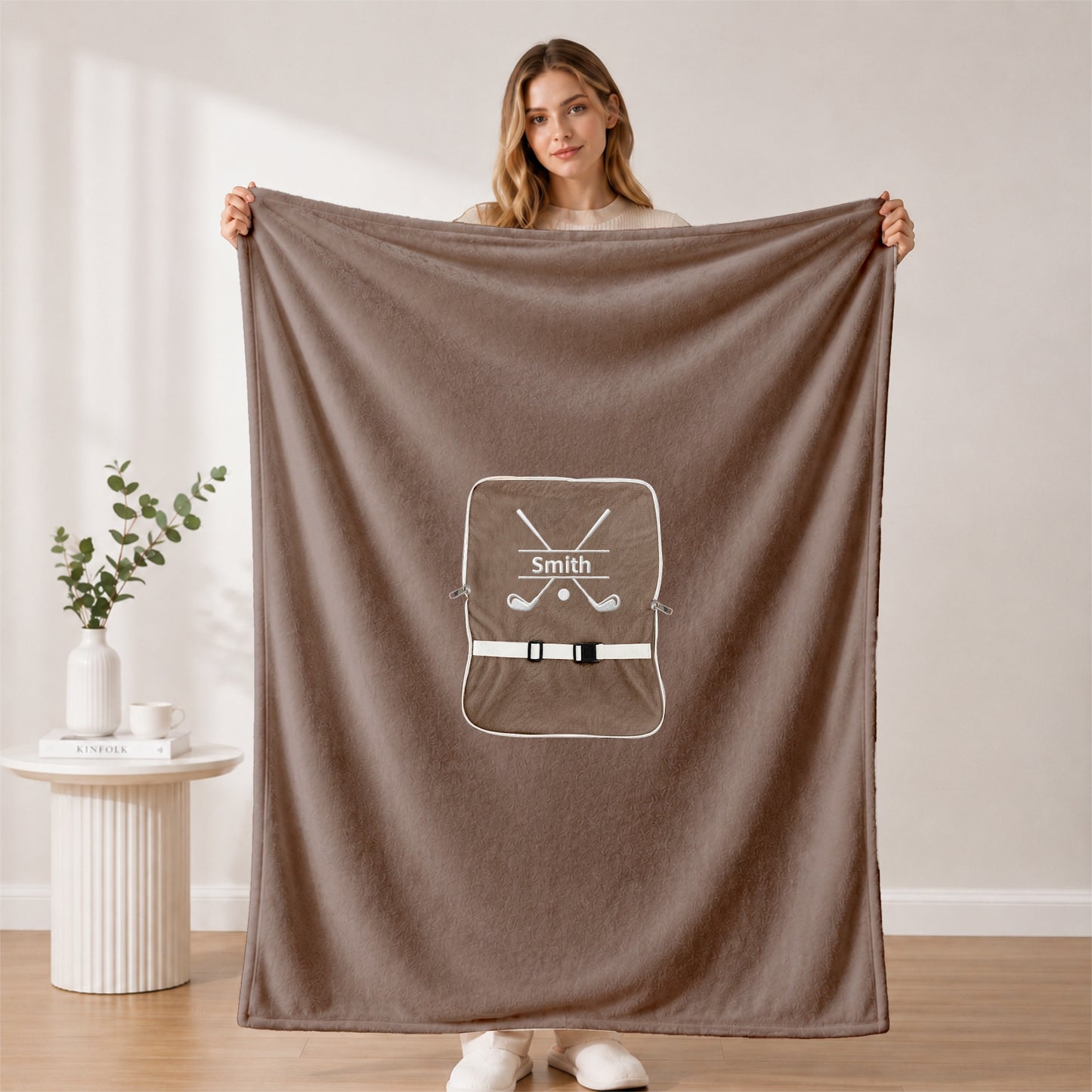Woman holding open dark green golf-themed blanket.