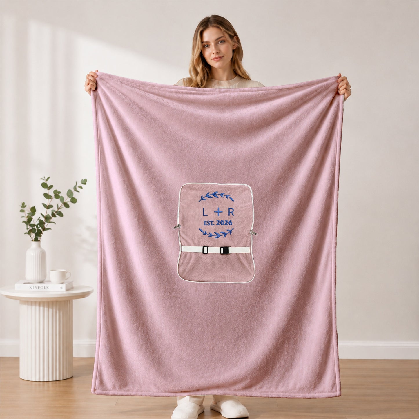 Woman holding open beige blanket with embroidered initials.
