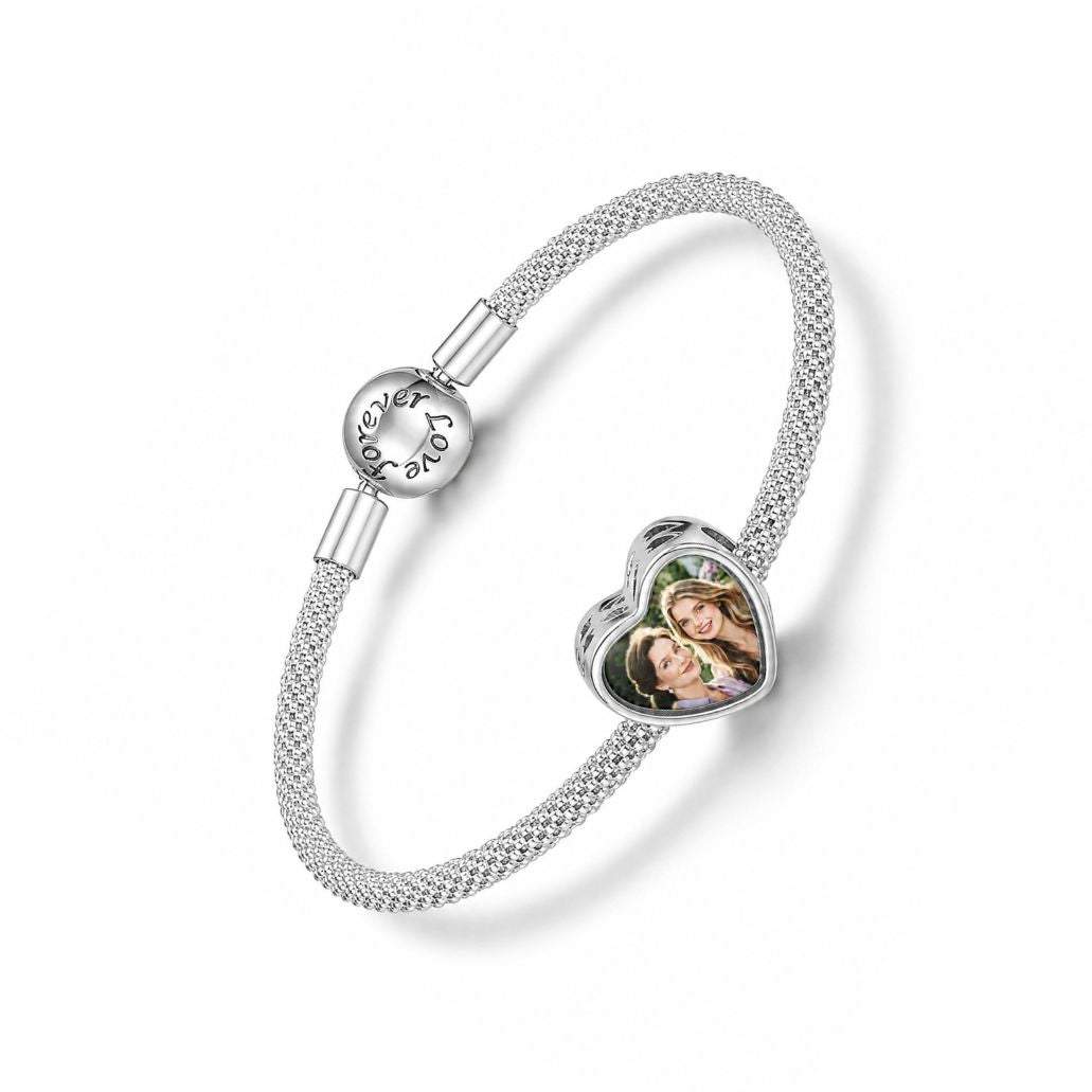 A silver mesh charm bracelet featuring a custom heart-shaped photo charm of two women and a spherical "forever love" clasp
