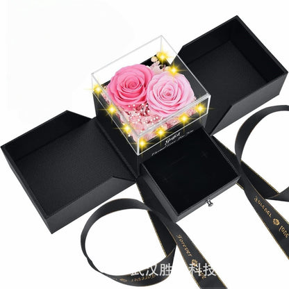 Two-tone pink preserved roses in a black gift box with gold-rimmed ribbon.