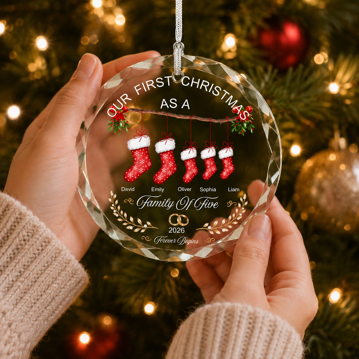 Personalized family Christmas ornament held by hands in front of a cozy Christmas tree with warm holiday lights