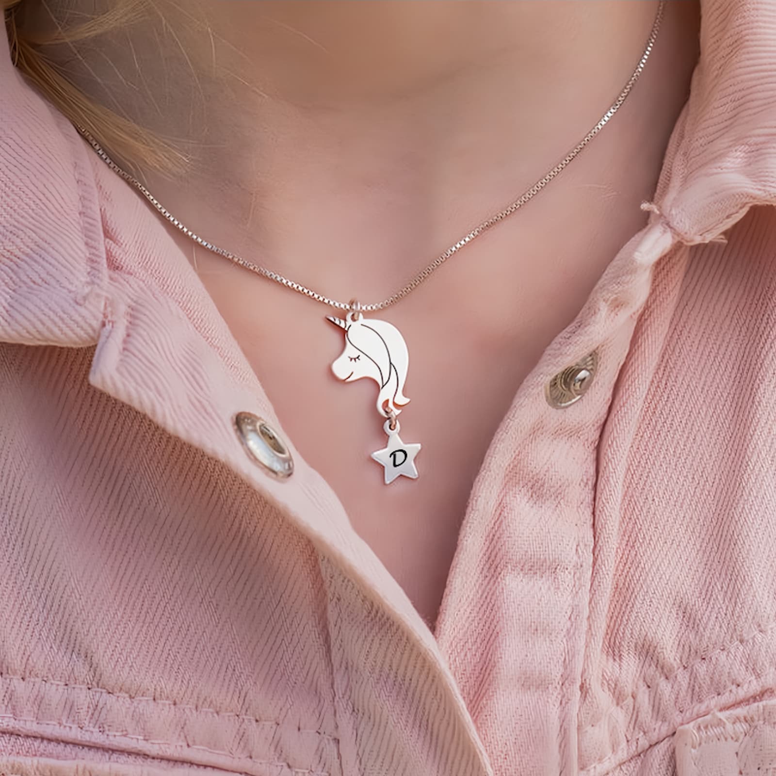 Close-up of a young girl wearing the silver personalized unicorn initial necklace on a pink jacket, showing the perfect size.