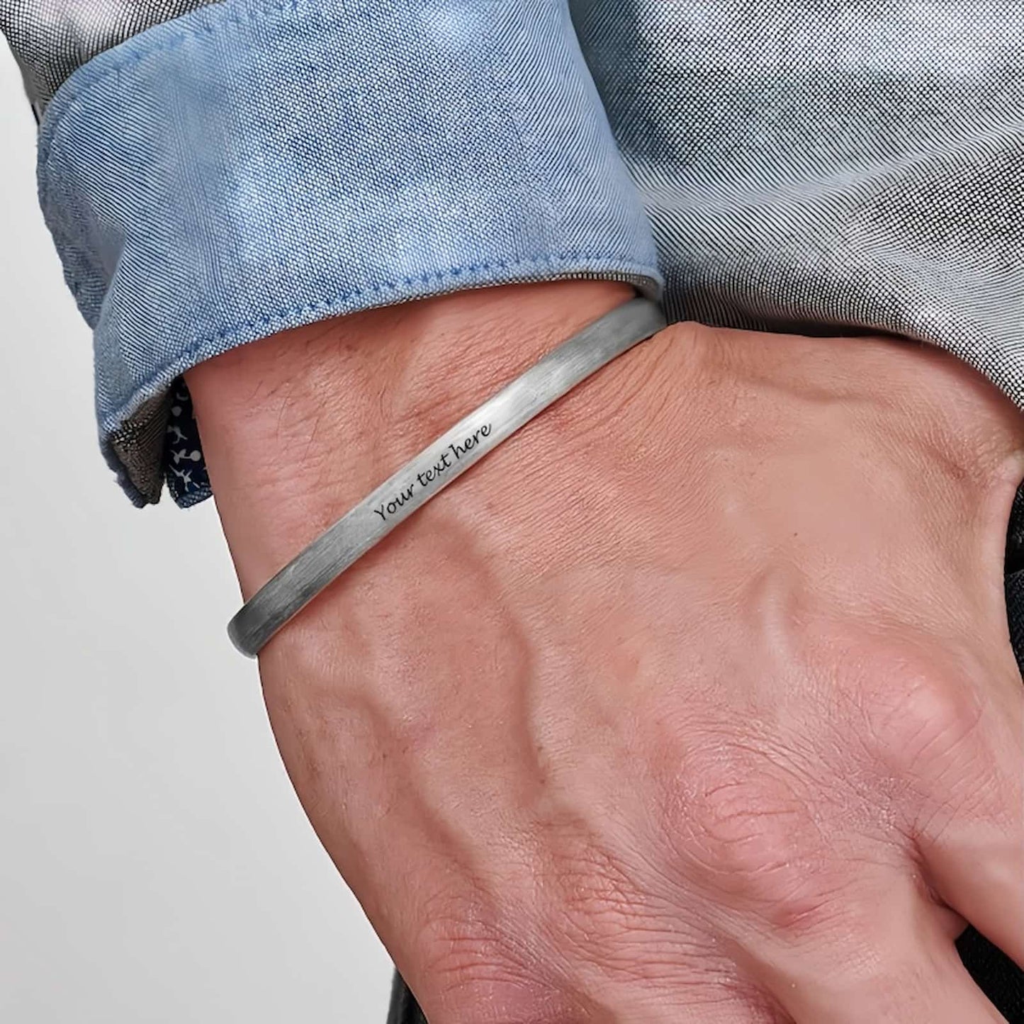Man wearing custom engraved silver cuff bracelet with braided texture, personalized text.