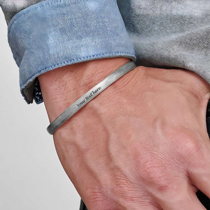Man wearing custom engraved silver cuff bracelet with braided texture, personalized text.