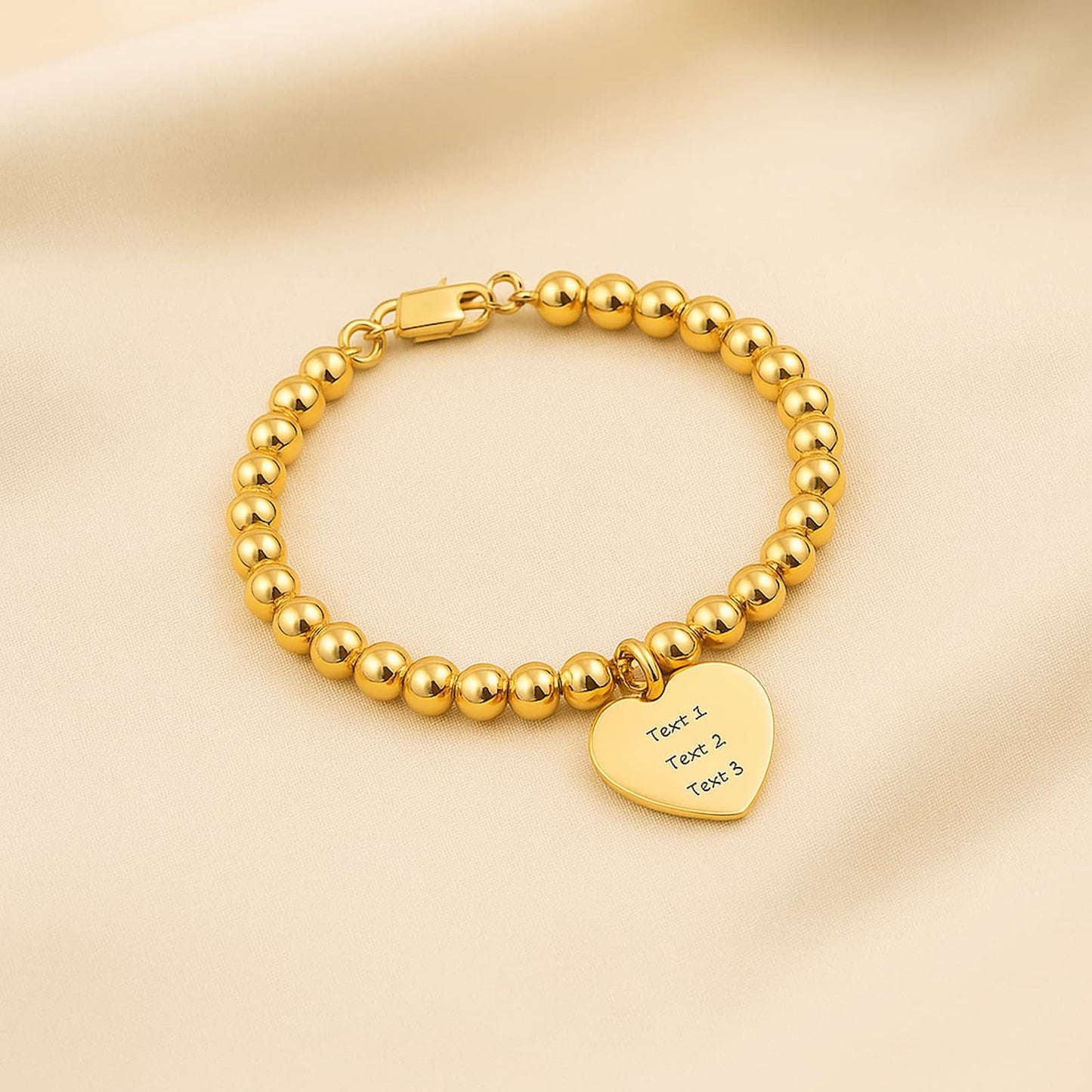 Gold bead ball strand bracelet with a custom heart charm, displayed on a soft, light-colored fabric backdrop.
