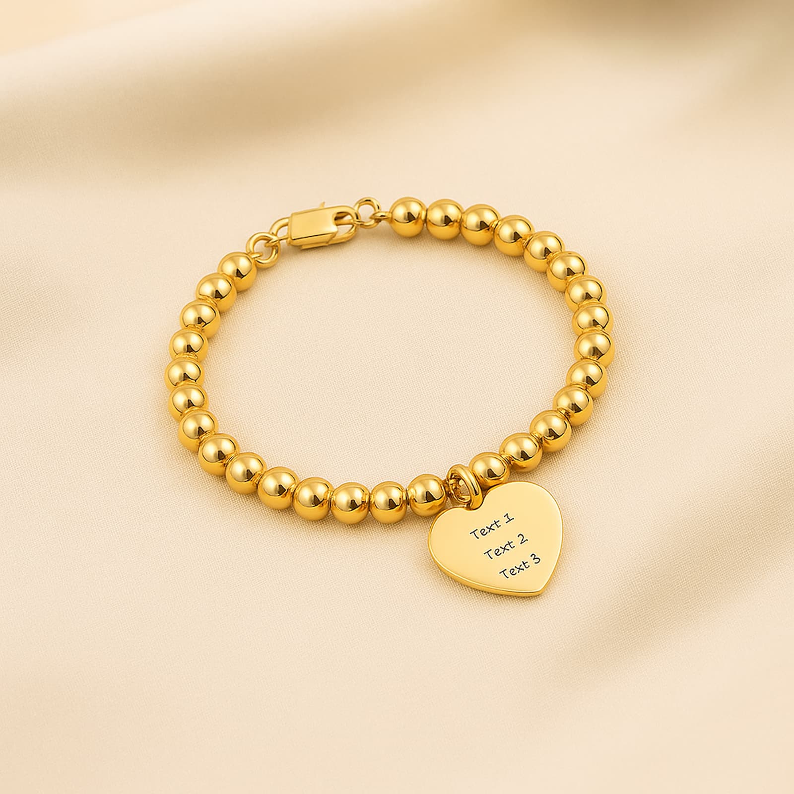 Gold bead ball strand bracelet with a custom heart charm, displayed on a soft, light-colored fabric backdrop.