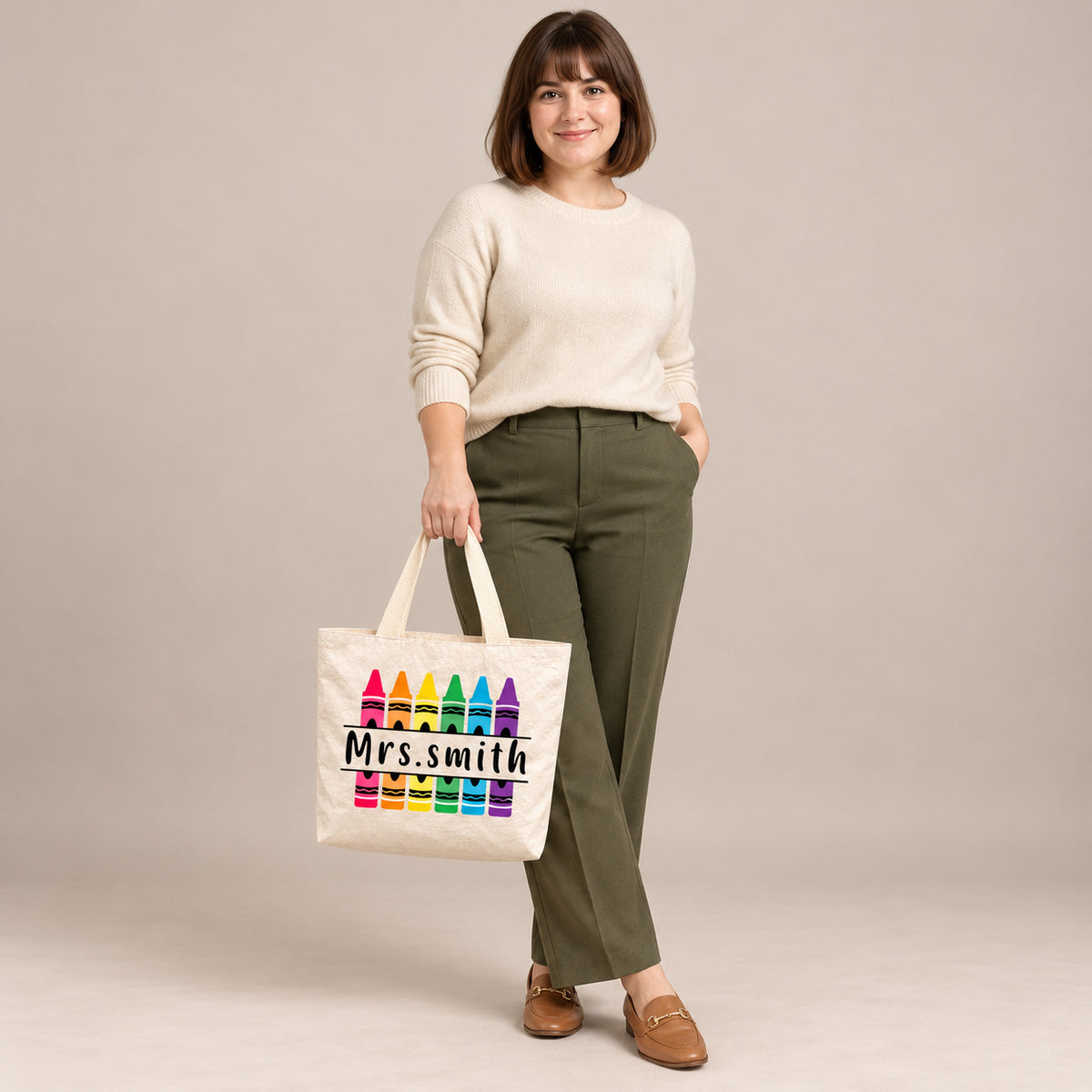 Personalized rainbow crayon teacher tote bag with custom name, carried by a model against a warm neutral backdrop.