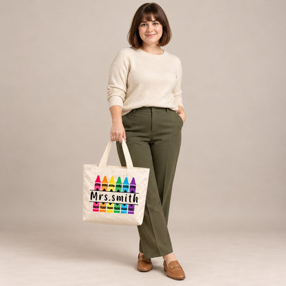 Personalized rainbow crayon teacher tote bag with custom name, carried by a model against a warm neutral backdrop.
