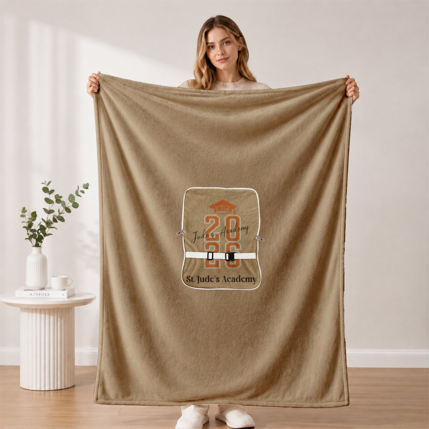 Woman holding full 2026 grad blanket in minimalist room.