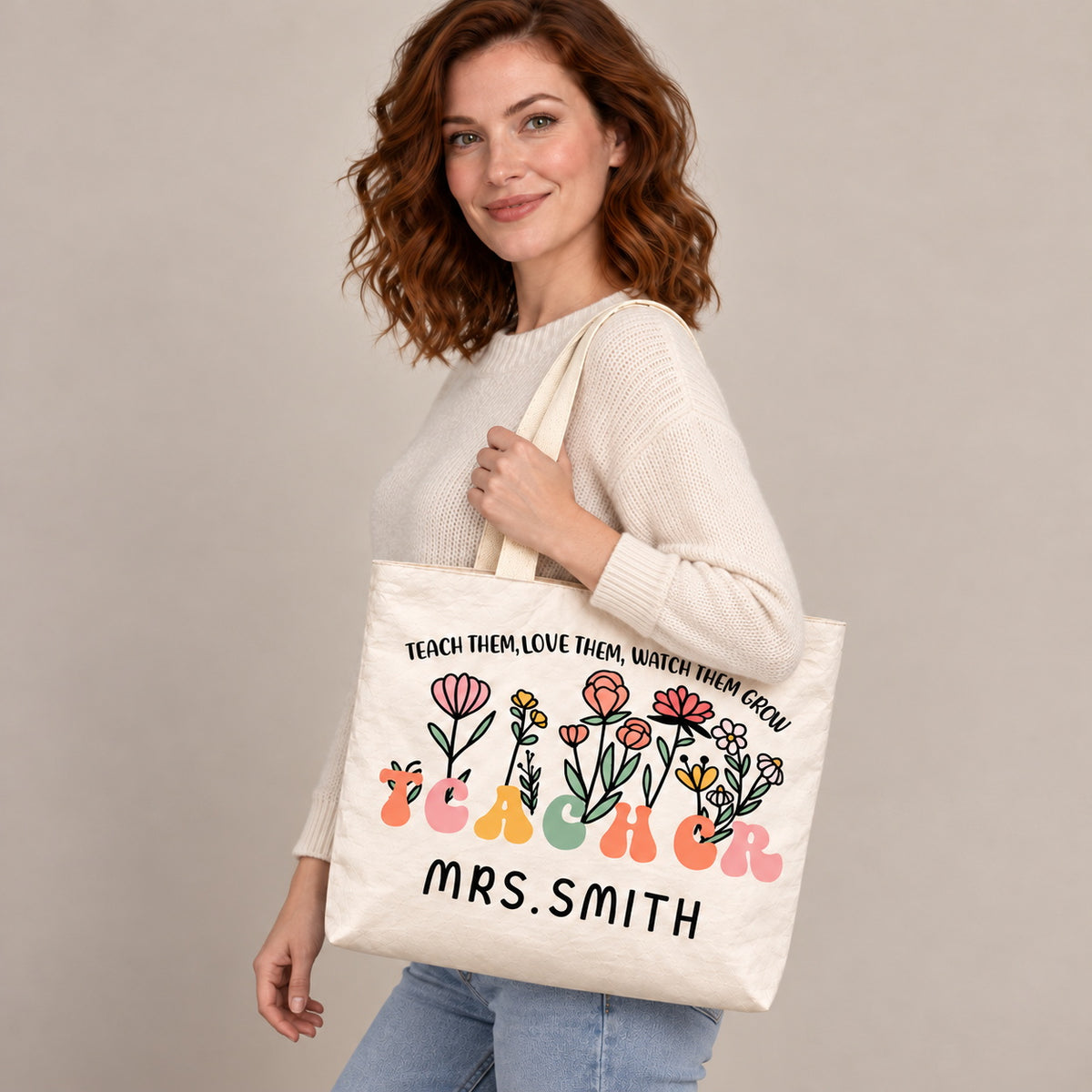 Personalized teacher tote with floral teacher artwork with the phrase TEACH THEM, LOVE THEM, WATCH THEM GROW and custom name MRS.SMITH, shoulder side view view.