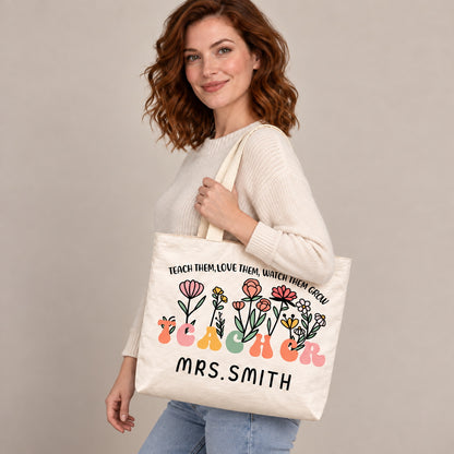 Personalized teacher tote with floral teacher artwork with the phrase TEACH THEM, LOVE THEM, WATCH THEM GROW and custom name MRS.SMITH, shoulder side view view.