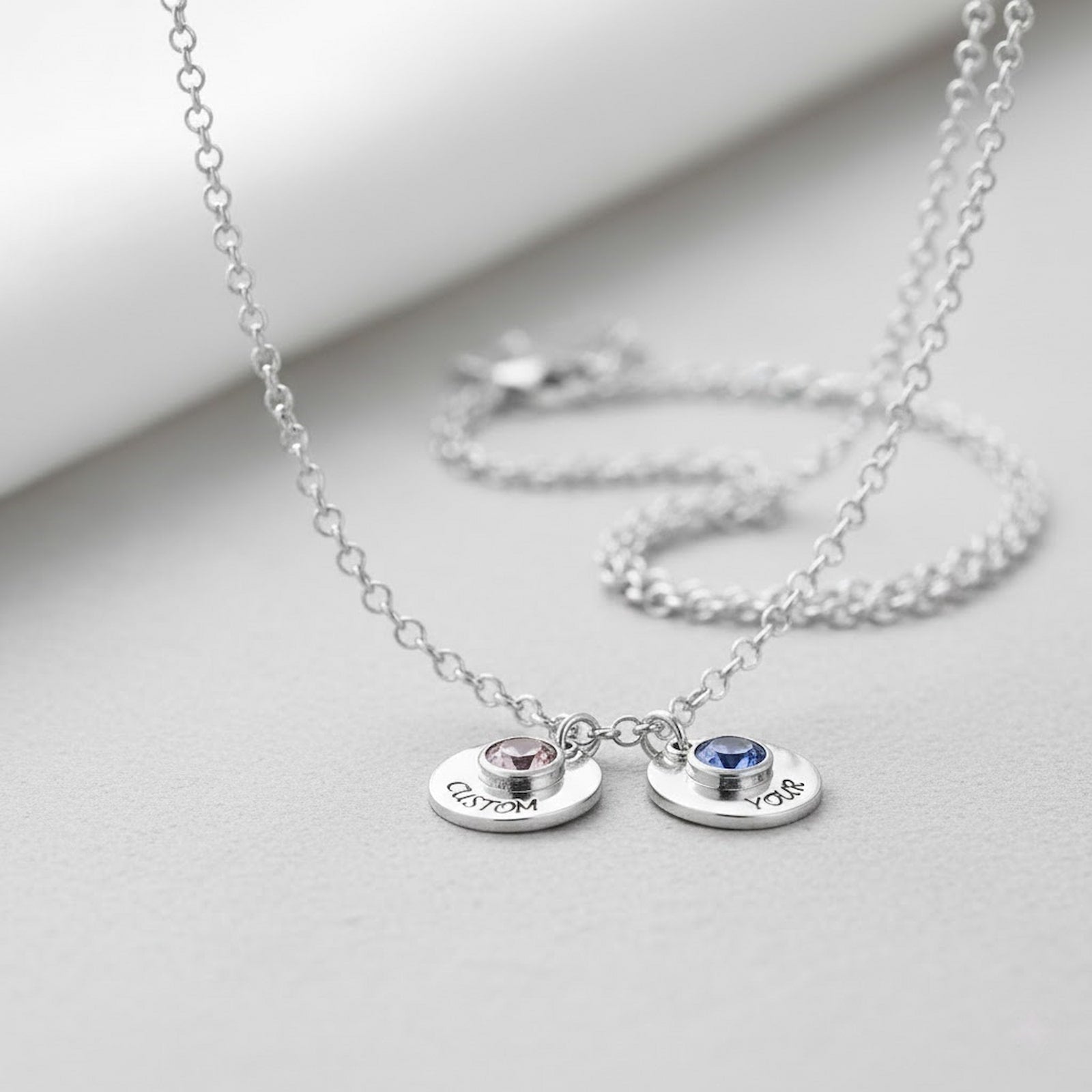 Two custom birthstone disc necklaces with personalized text in sterling silver.