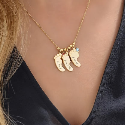Woman wearing gold baby foot name birthstone necklace.