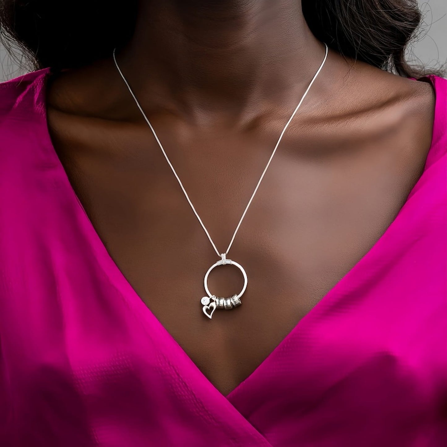 Model wearing the sterling silver personalized circle necklace with engraved charms over a pink dress, showing the long chain and layering effect.
