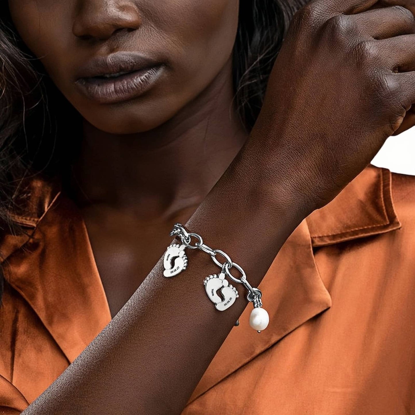 Woman wearing silver baby footprint name bracelet with engraved names, dates & pearl charm.