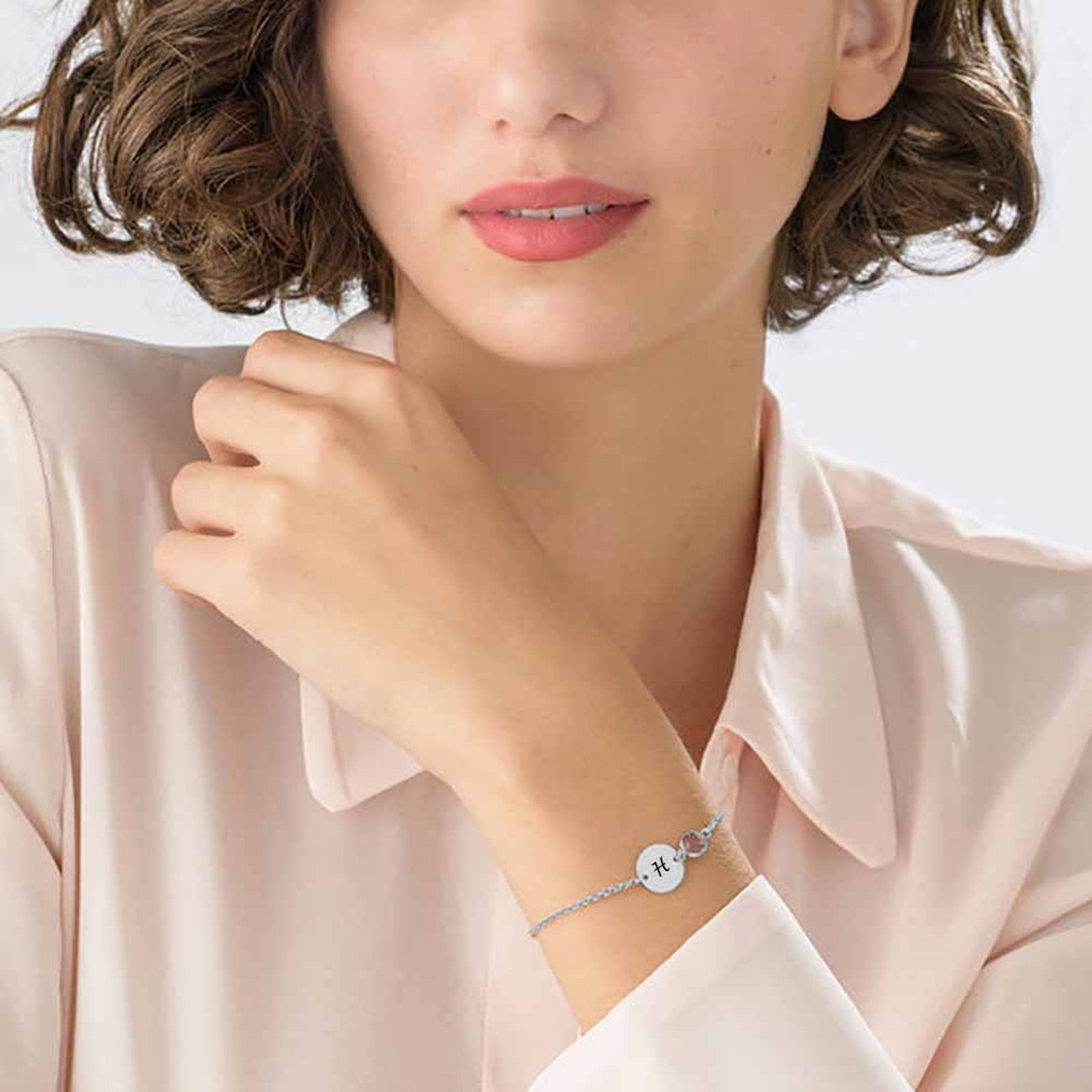 Woman wearing silver personalized initial disc bracelet with birthstone, engraved letter.