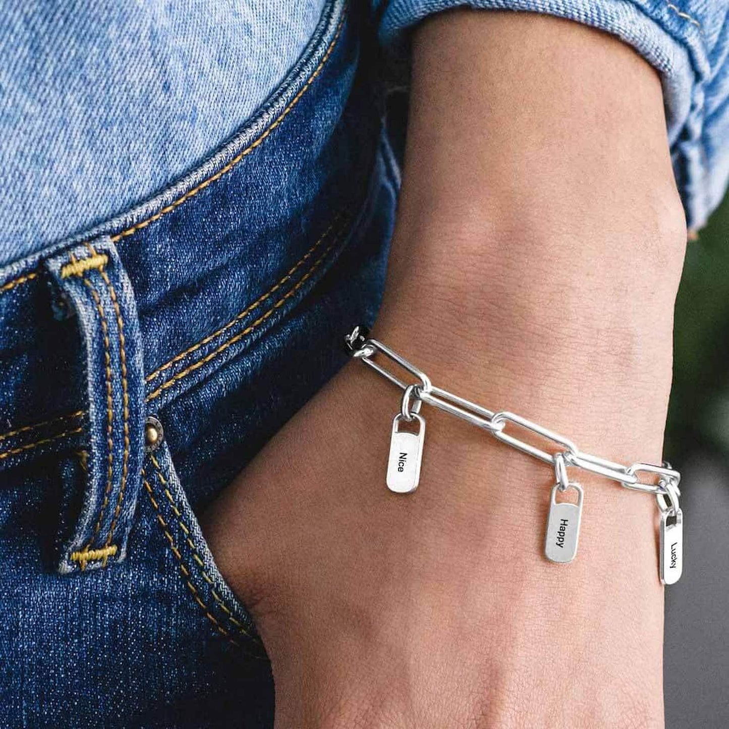 Woman wearing silver personalized paperclip bracelet with custom engraved charms on wrist.