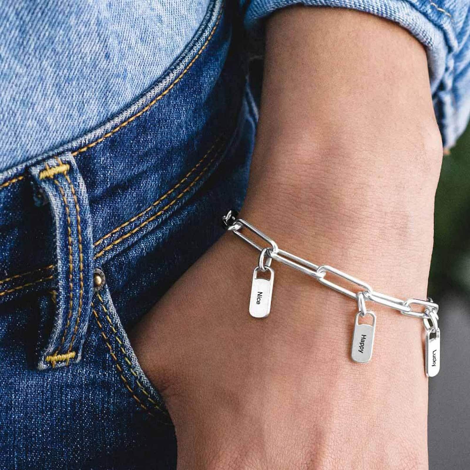 Woman wearing silver personalized paperclip bracelet with custom engraved charms on wrist.